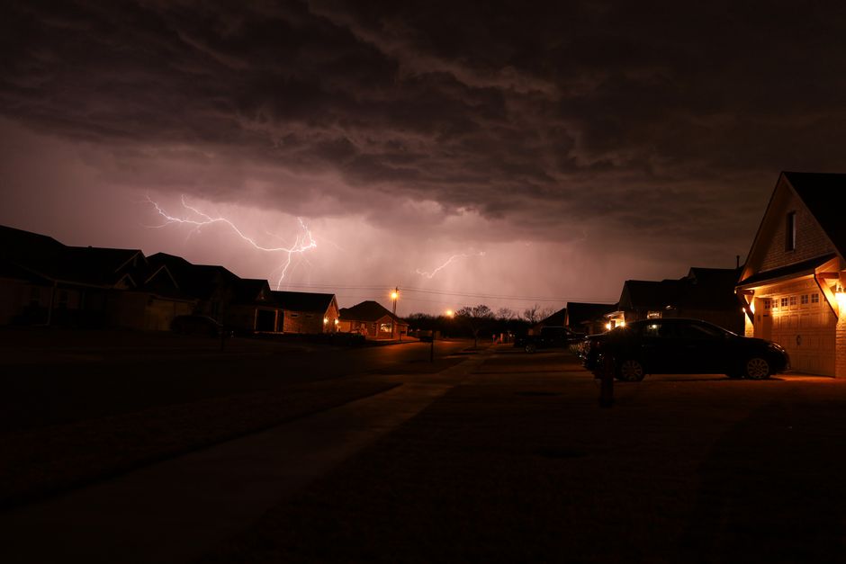 A night-time thunderstorm with lightning over a residential street.