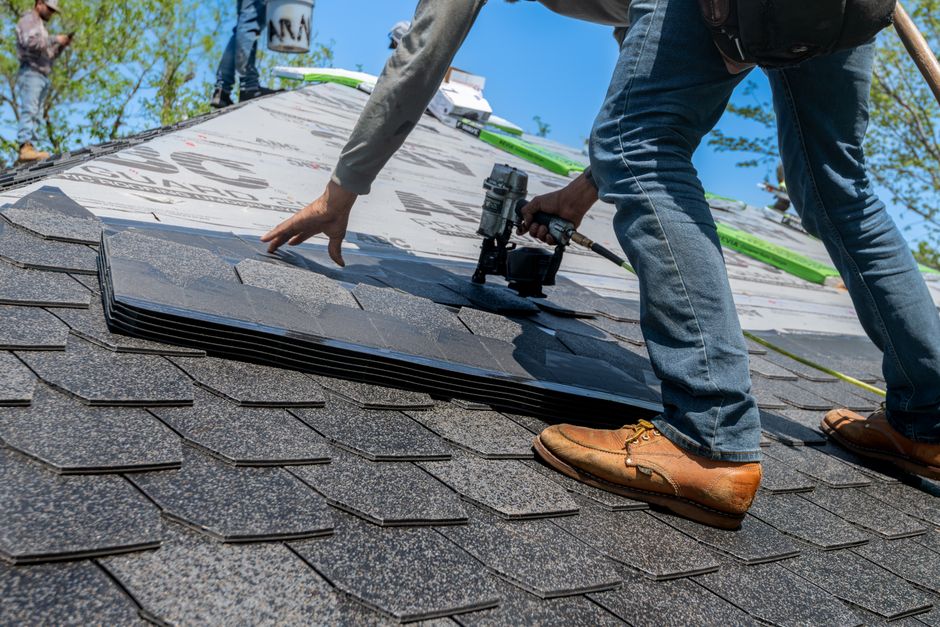 A roofer using a nail gun to fasten shingles on a new roof.
