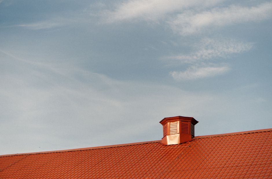 A vent on a red metal roof against a clear blue sky.